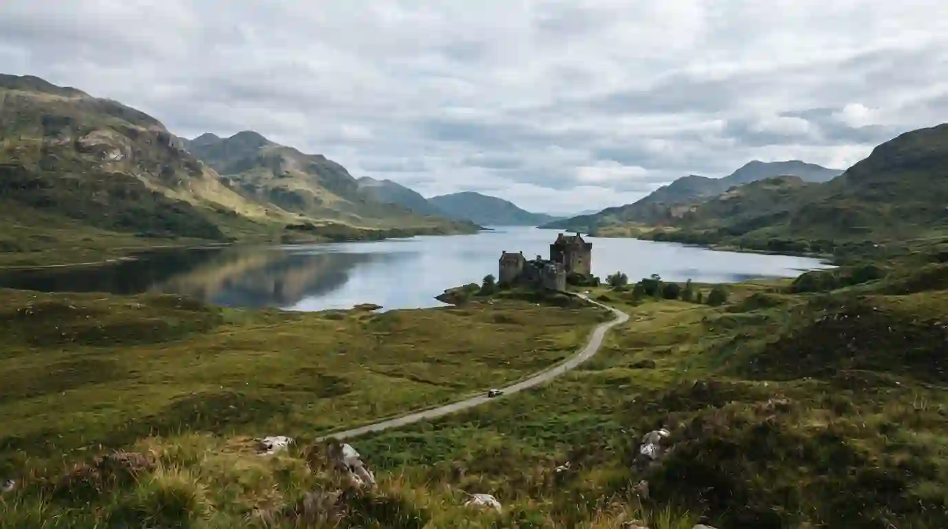 Scottish Highland landscape with a loch, rugged mountains, winding road, and historic stone castle